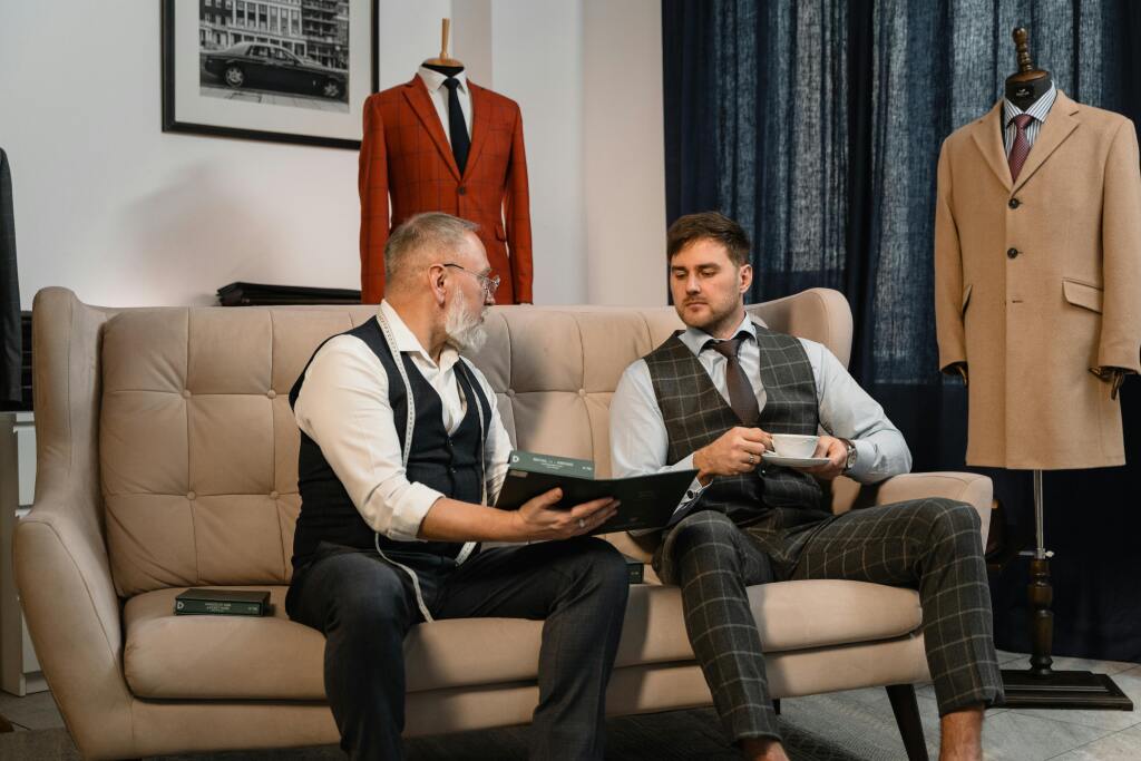 Hommes portant gilets vintage à carreaux et costumes sur mesure dans atelier de tailleur avec vestes rétro terracotta et beige en arrière-plan